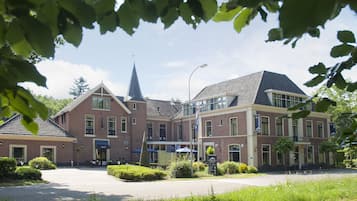 Stately brick building with a central entrance, surrounded by lush greenery and a paved driveway.