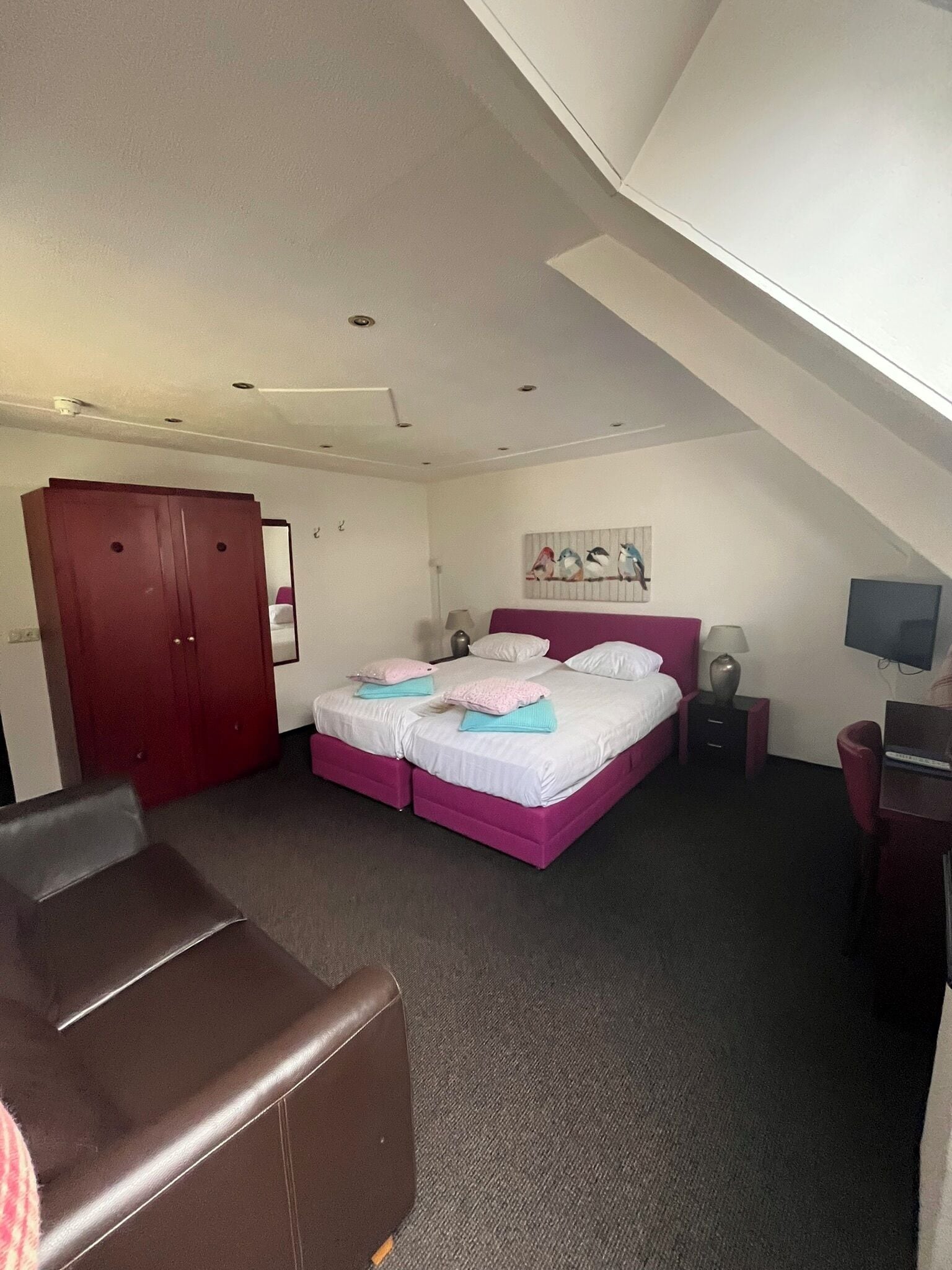 A bedroom with a bed, a desk, a chair, a wardrobe, and a painting on the wall.