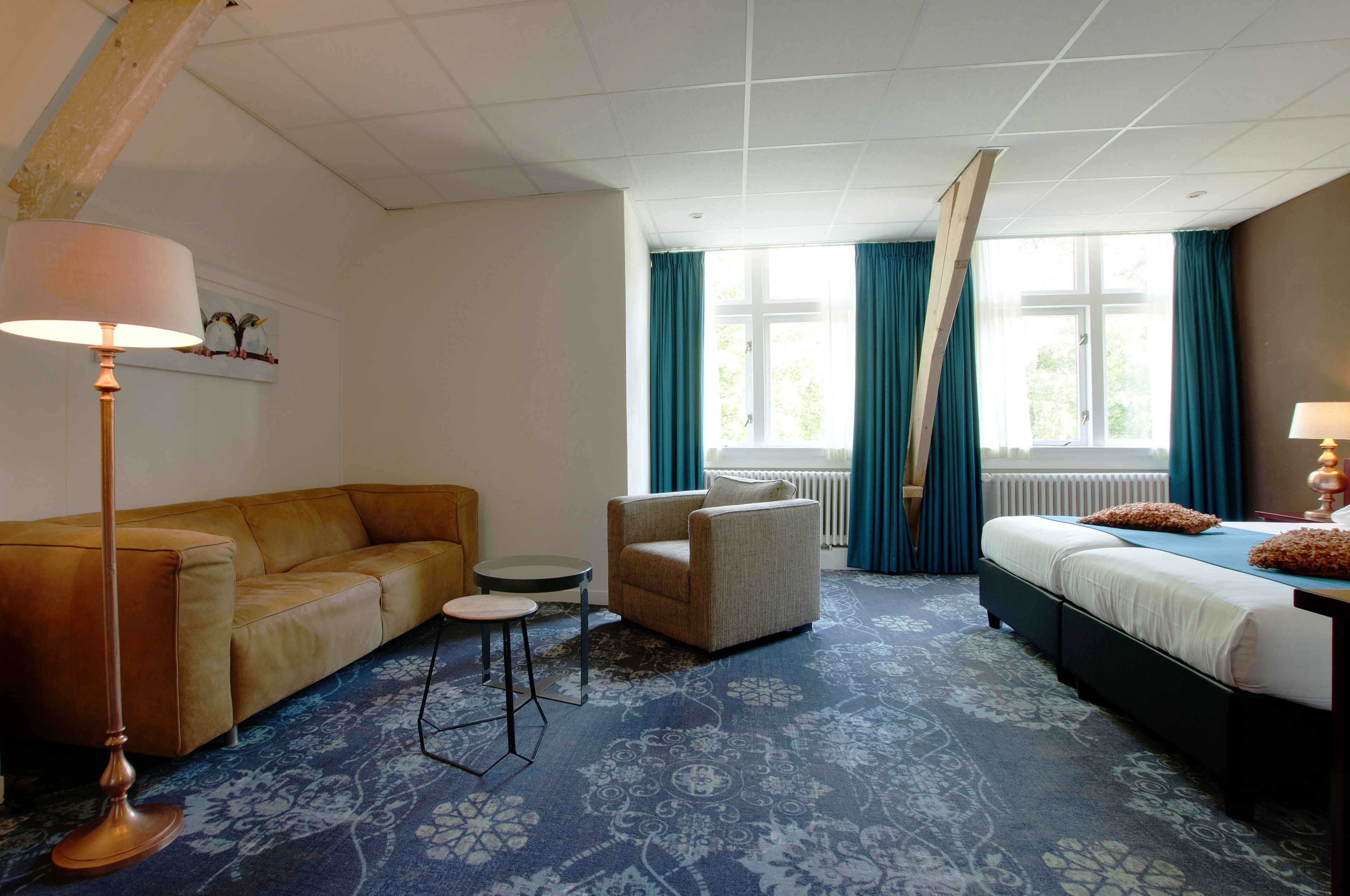 Habitación de hotel con sofá, sillón, mesita redonda y cama con cabecera.