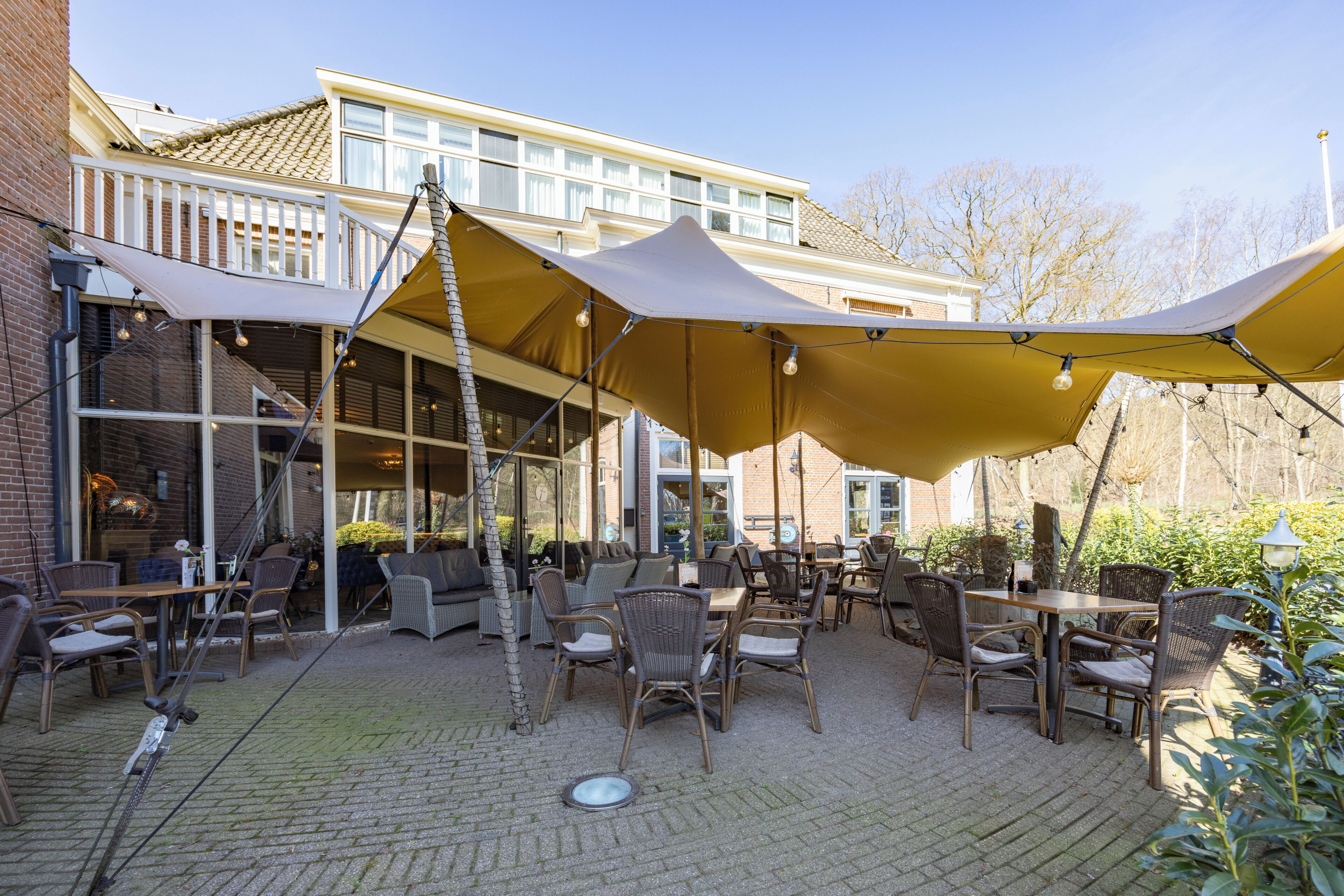 Un espace extérieur aménagé en terrasse, avec des tables et des chaises, de grands parasols et un bâtiment en briques en arrière-plan.