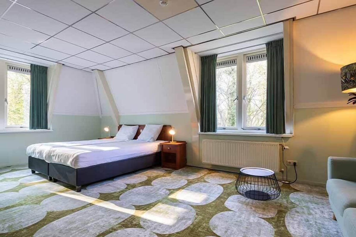 Un dormitorio con cama, mesita de noche, lámpara y vistas al exterior a través de una ventana.