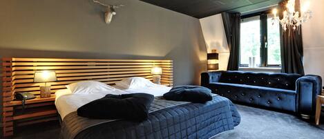 A modern hotel room with a large bed, a sofa, a chandelier, and a window with curtains.