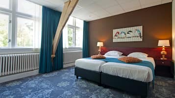 A double bed with two pillows, a blue and white patterned carpet, a wooden headboard, a painting of birds on the wall, and two bedside lamps.