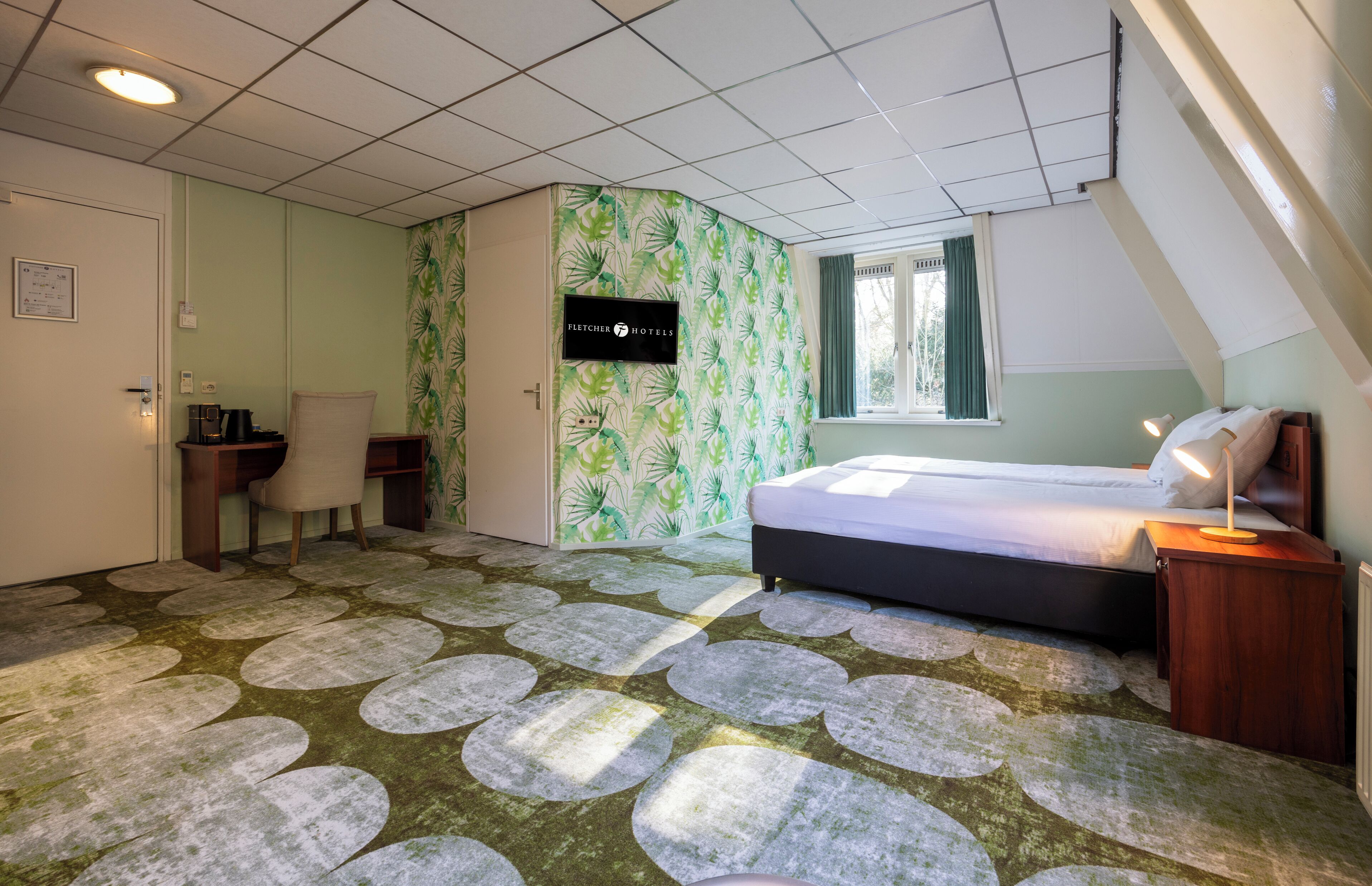 Ein Schlafzimmer mit einem Bett, einem Nachttisch, einem Sessel, einem Schreibtisch, einem Fenster und einer Wand mit grünem Muster.