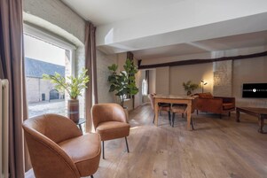 A modern hotel room with a wooden floor, a dining area with a table and chairs, and large windows with curtains.