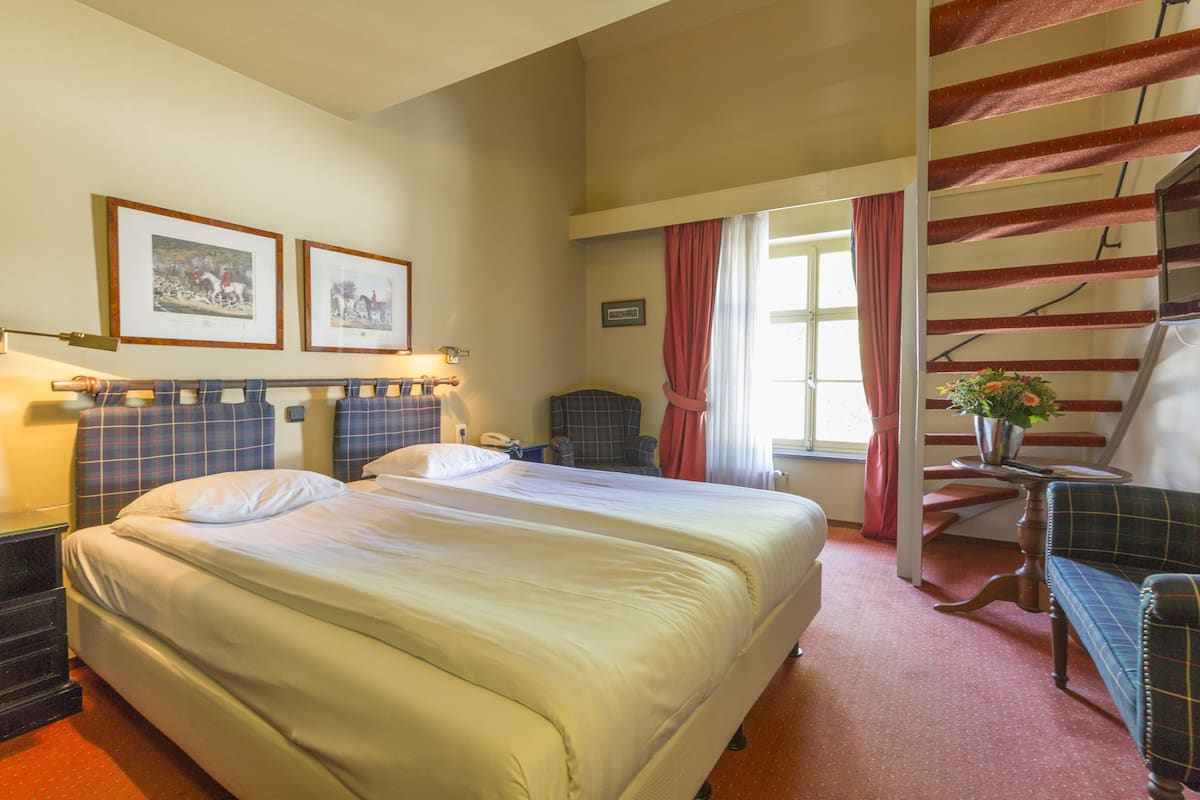 Une chambre d’hôtel avec un grand lit, une chaise, un bureau et un escalier.