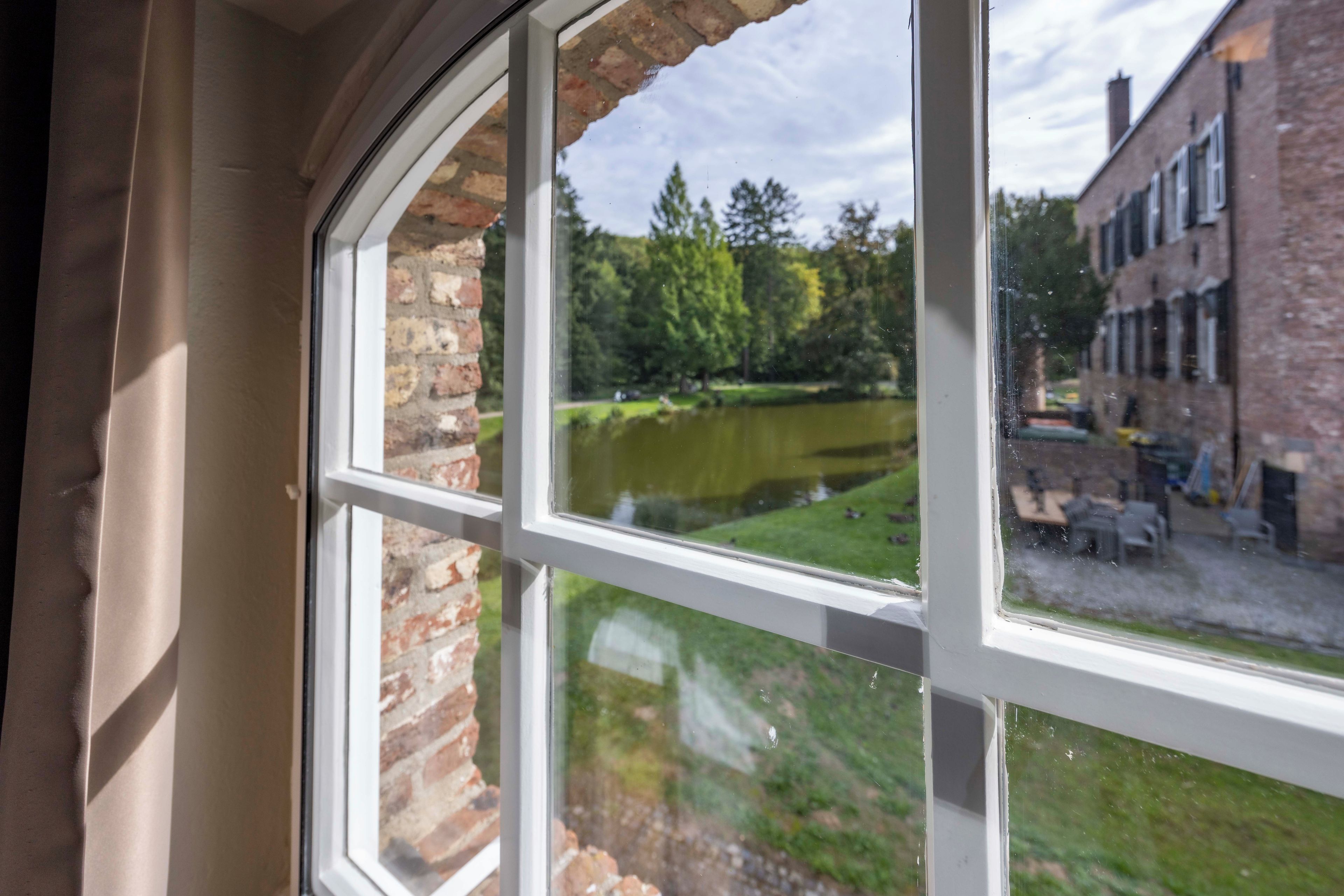 Ventana con vista a un estanque, un muro de ladrillo y un edificio con techo inclinado.