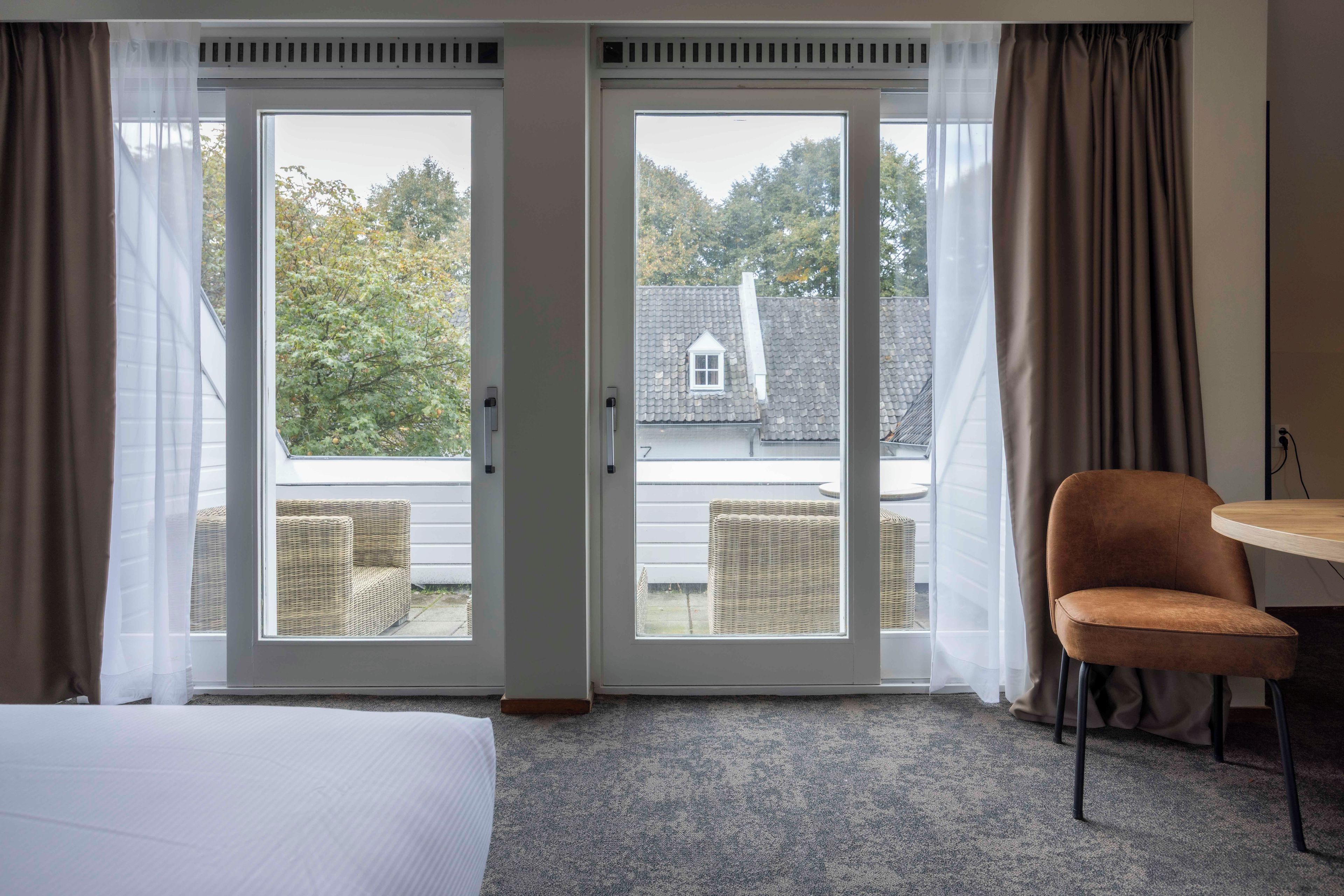 Ein Hotelzimmer mit einem Bett, einem Sessel und Blick auf ein Haus durch eine Schiebetür.