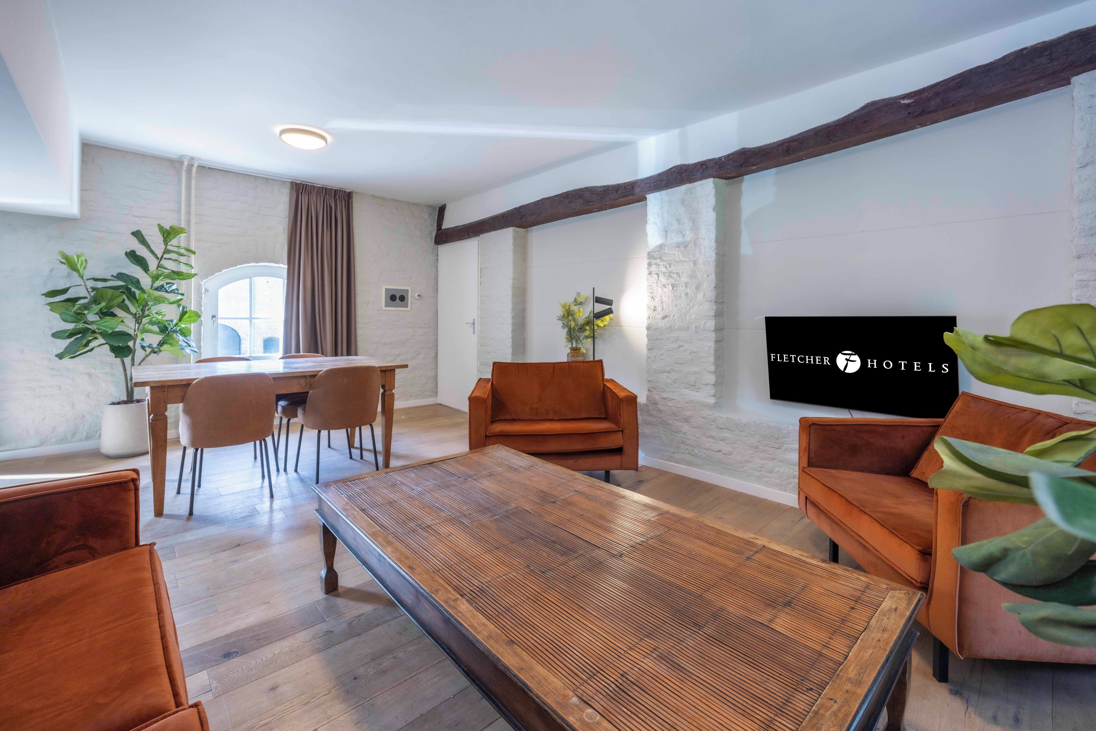Ein modernes Wohnzimmer mit Holztisch, zwei Sofas, einer Essecke mit Stühlen und einem großen Fernsehbildschirm.