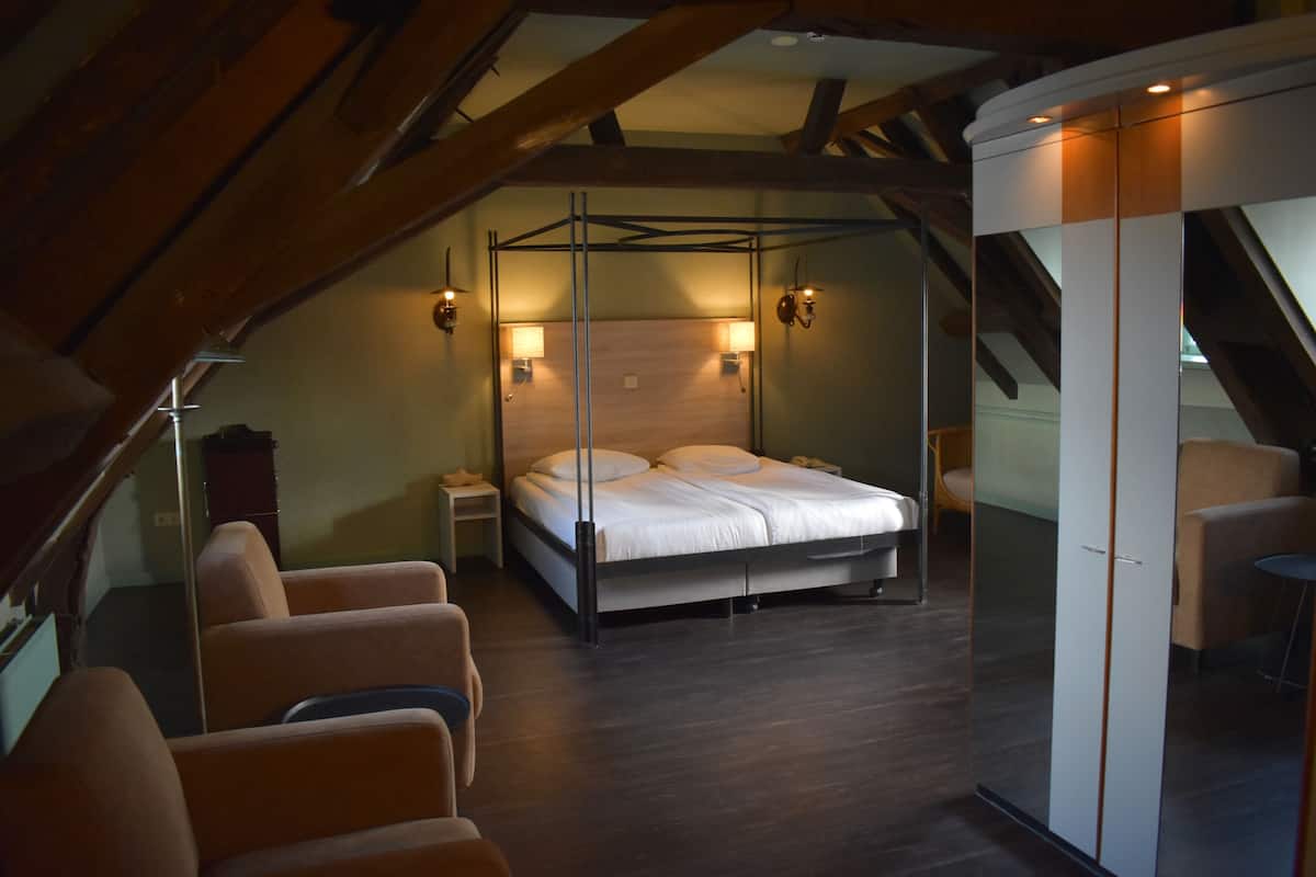 Une chambre à coucher avec un lit à baldaquin, un coin salon avec des fauteuils et un escalier.