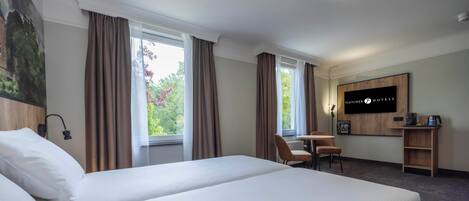 Habitación de hotel con una cama grande, un escritorio con silla, un televisor y vistas a zonas verdes.