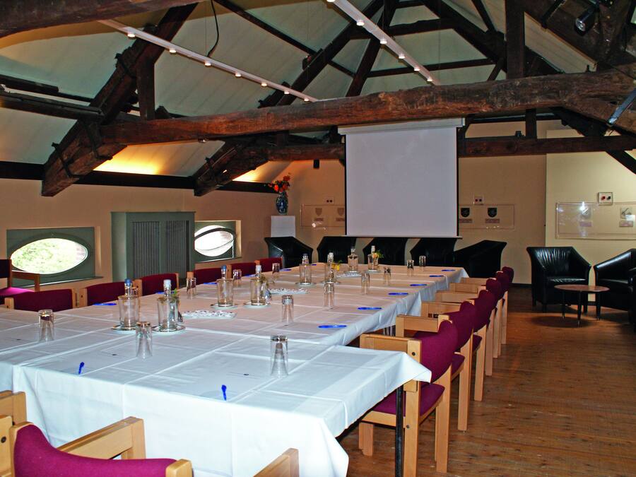 A long dining table set with chairs, a projector screen, and a wooden ceiling structure.