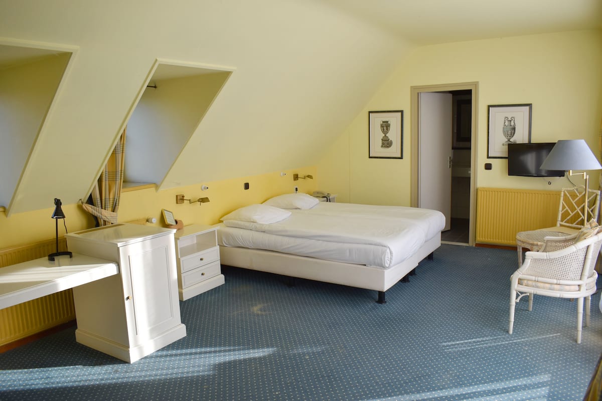 Une chambre à coucher comprenant un lit, un bureau, une chaise, un téléviseur et une porte donnant sur une autre pièce.
