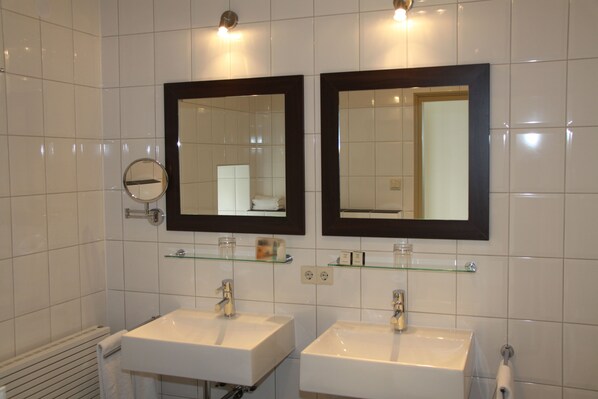 A bathroom with two sinks, a mirror above each, and a glass shelf between them.