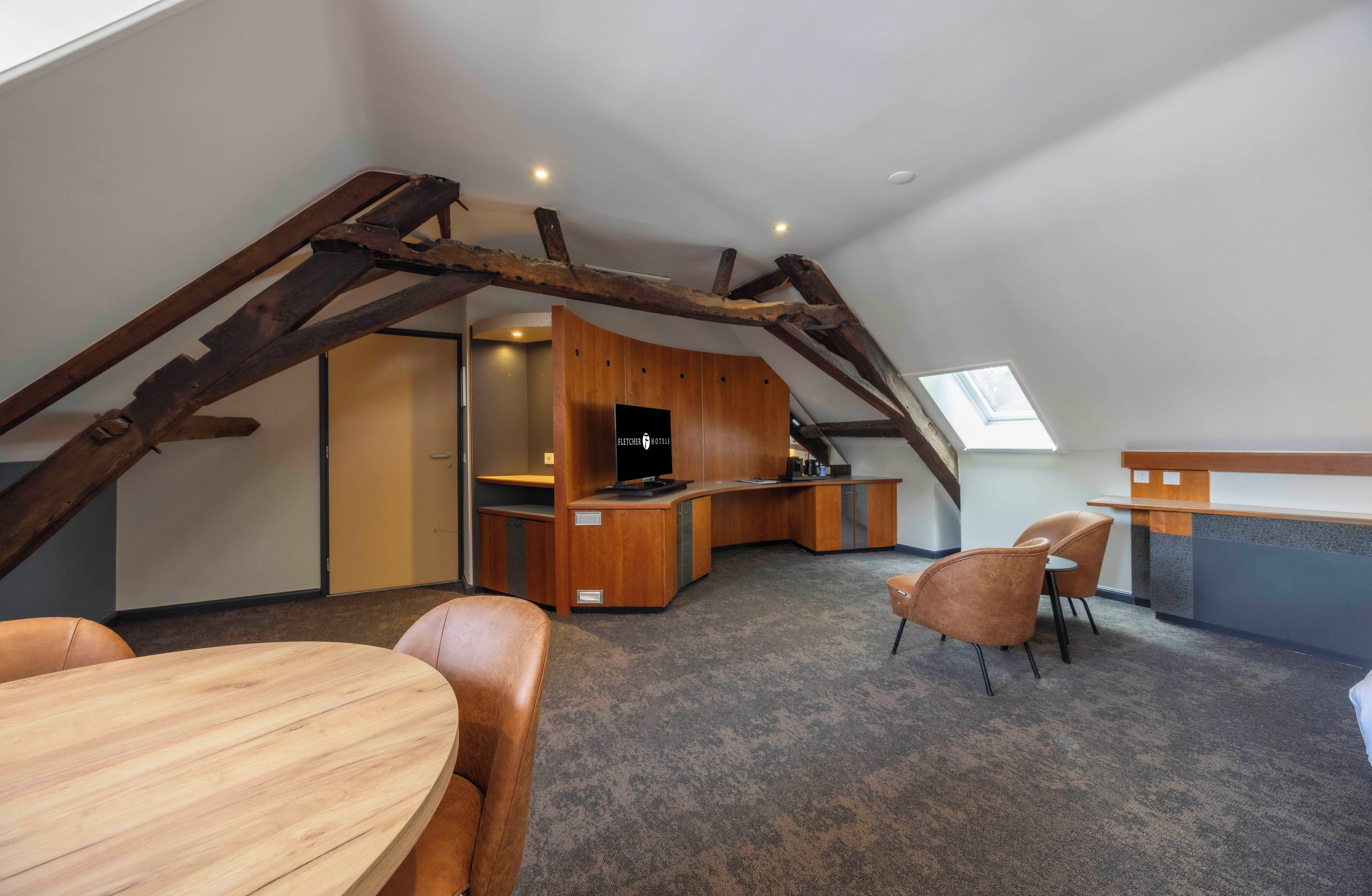 Een loft-achtige kamer met een houten bureau, een televisie en een zithoek.