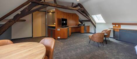 Een loft-achtige kamer met een houten bureau, een televisie en een zithoek.