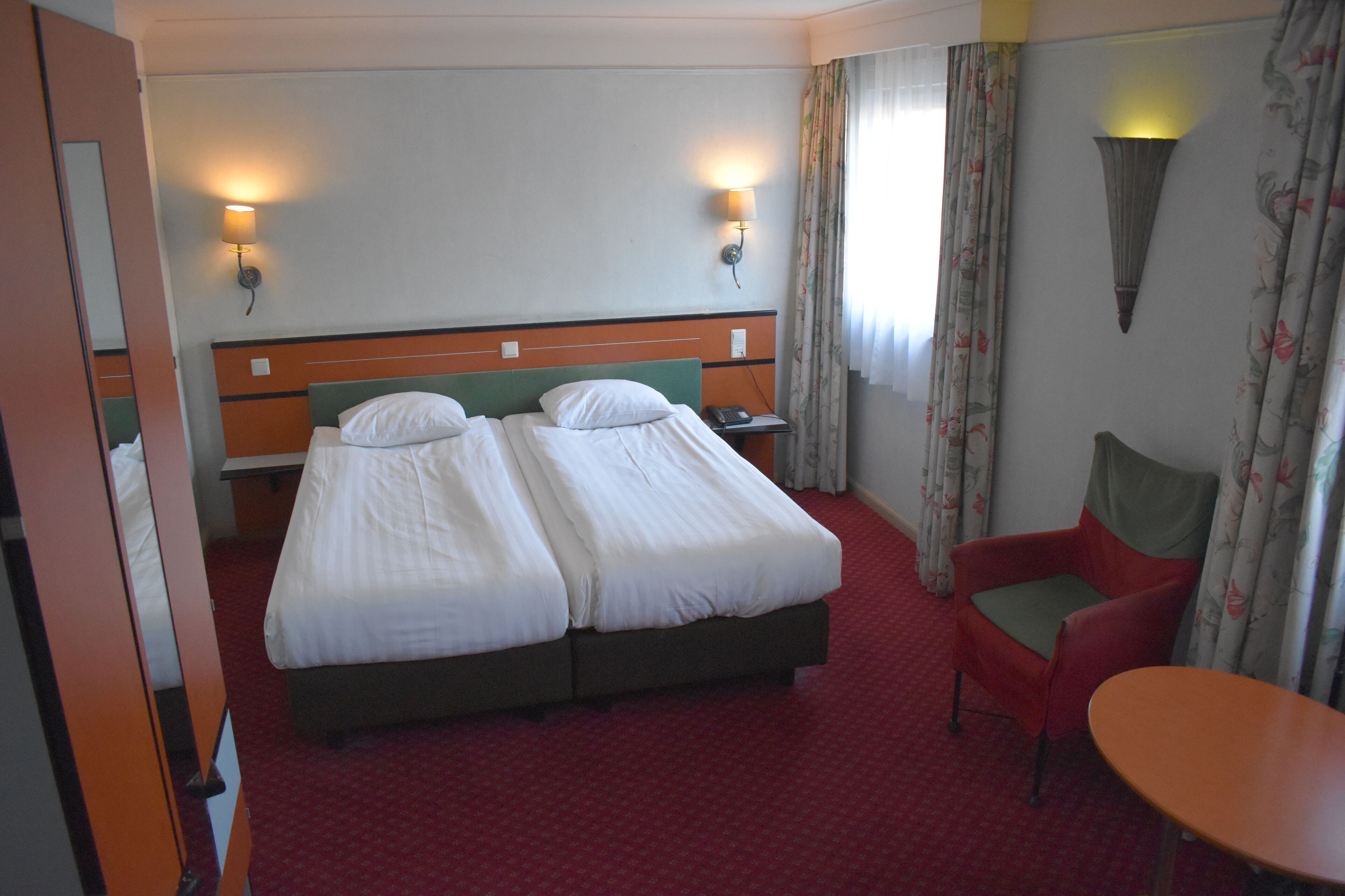 A hotel room with a double bed, two bedside lamps, a chair, a table, and a mirror.
