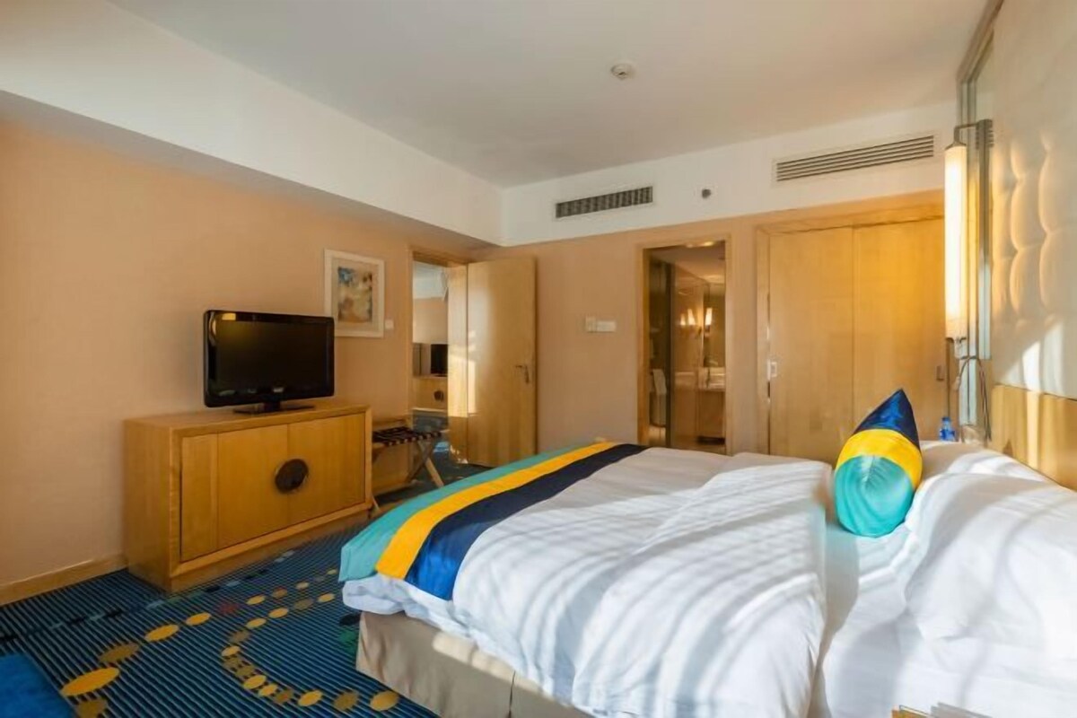 Una habitación de hotel con cama, televisión sobre un mueble de madera, puerta de baño y espejo.