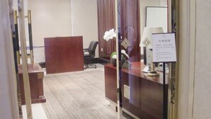 An office space with a reception desk, a black office chair, a potted plant, and a sign with contact information. - Jinling Mingdu Hotel Changzhou (Changzhou)