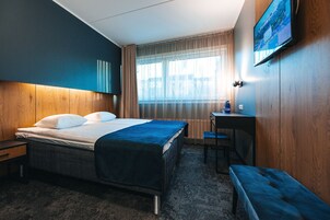 Ein Hotelzimmer mit einem Bett, einem Schreibtisch, einer Bank und einem an der Wand montierten Fernseher.