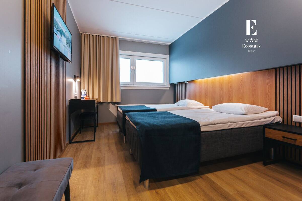 A modern hotel room with a large bed, a desk, and a TV mounted on the wall.