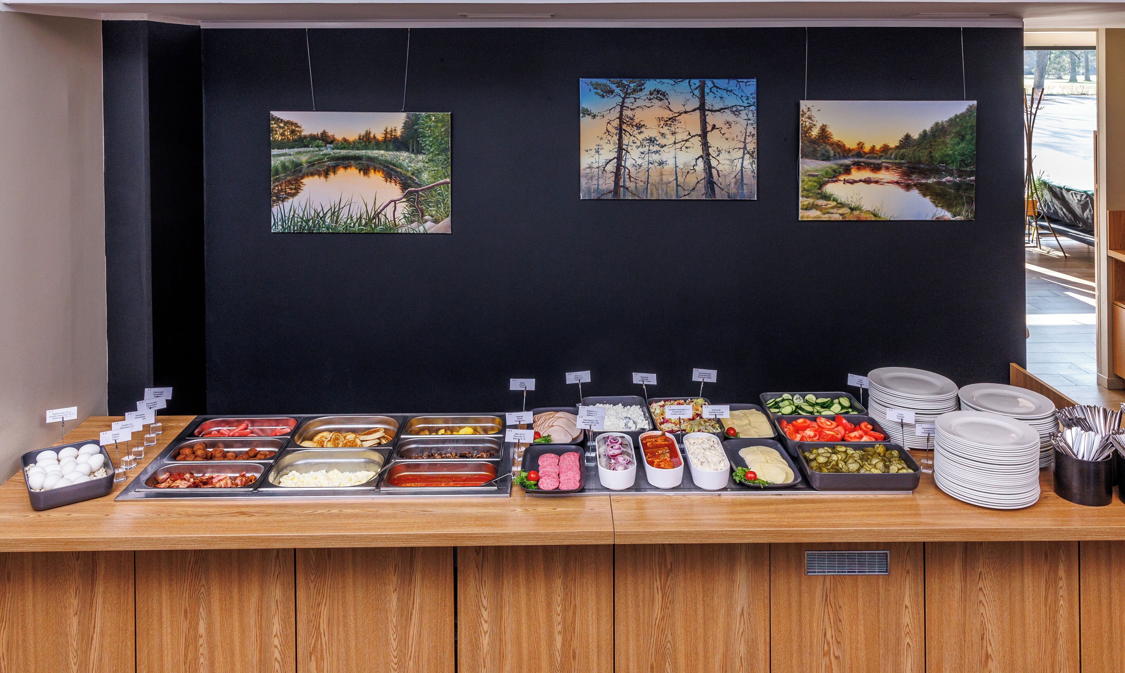Un buffet proposant une variété de plats et trois tableaux représentant des paysages accrochés au mur.