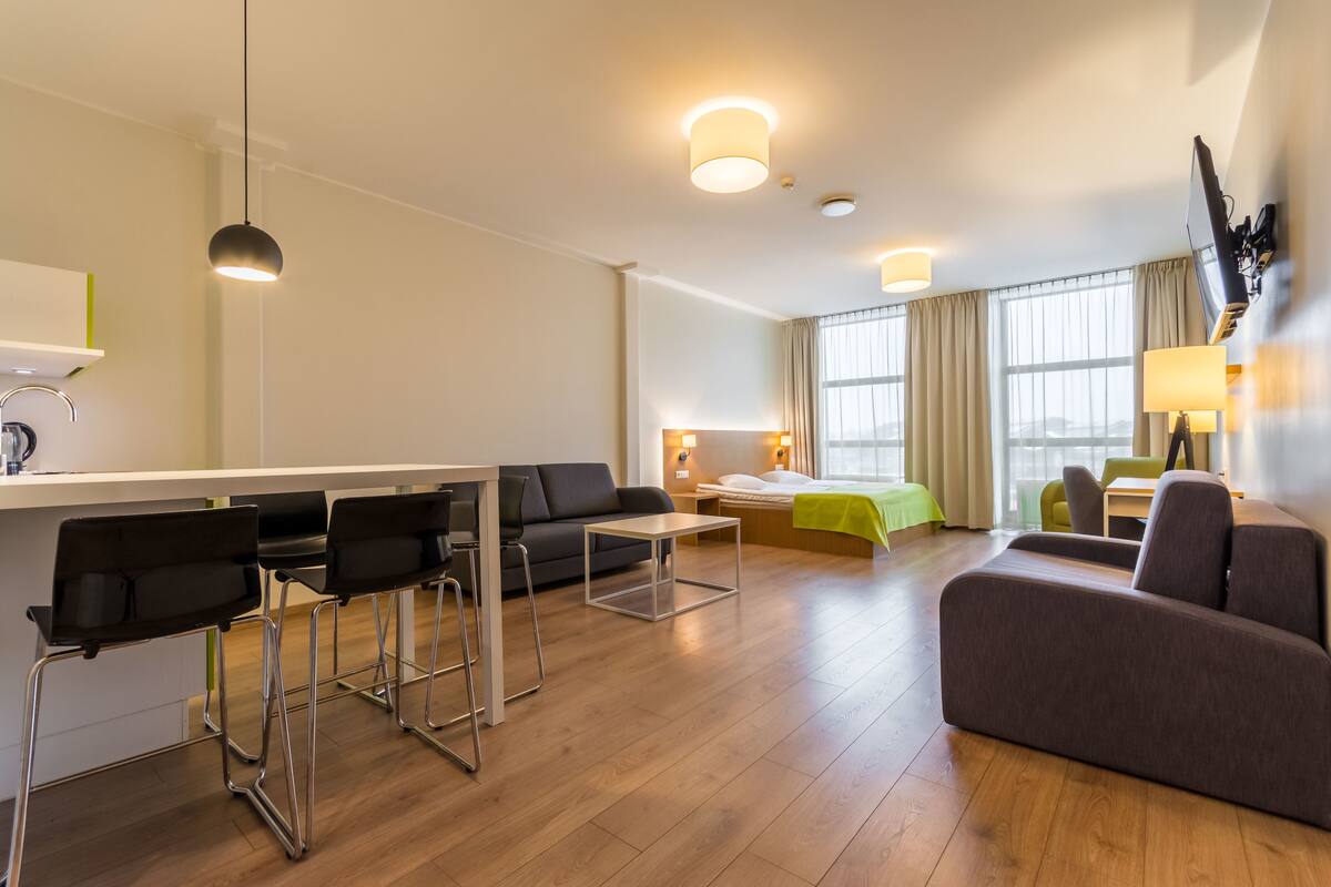 A modern hotel room with a dining area, a sofa, a bed, and a TV mounted on the wall.