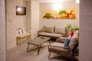 Una habitación acogedora con un sofá, una mesita, un banco y un televisor colocado en la pared.
