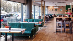 A modern cafe with green sofas, wooden tables, and a bar area. - Go Hotel Shnelli (Tallinn)