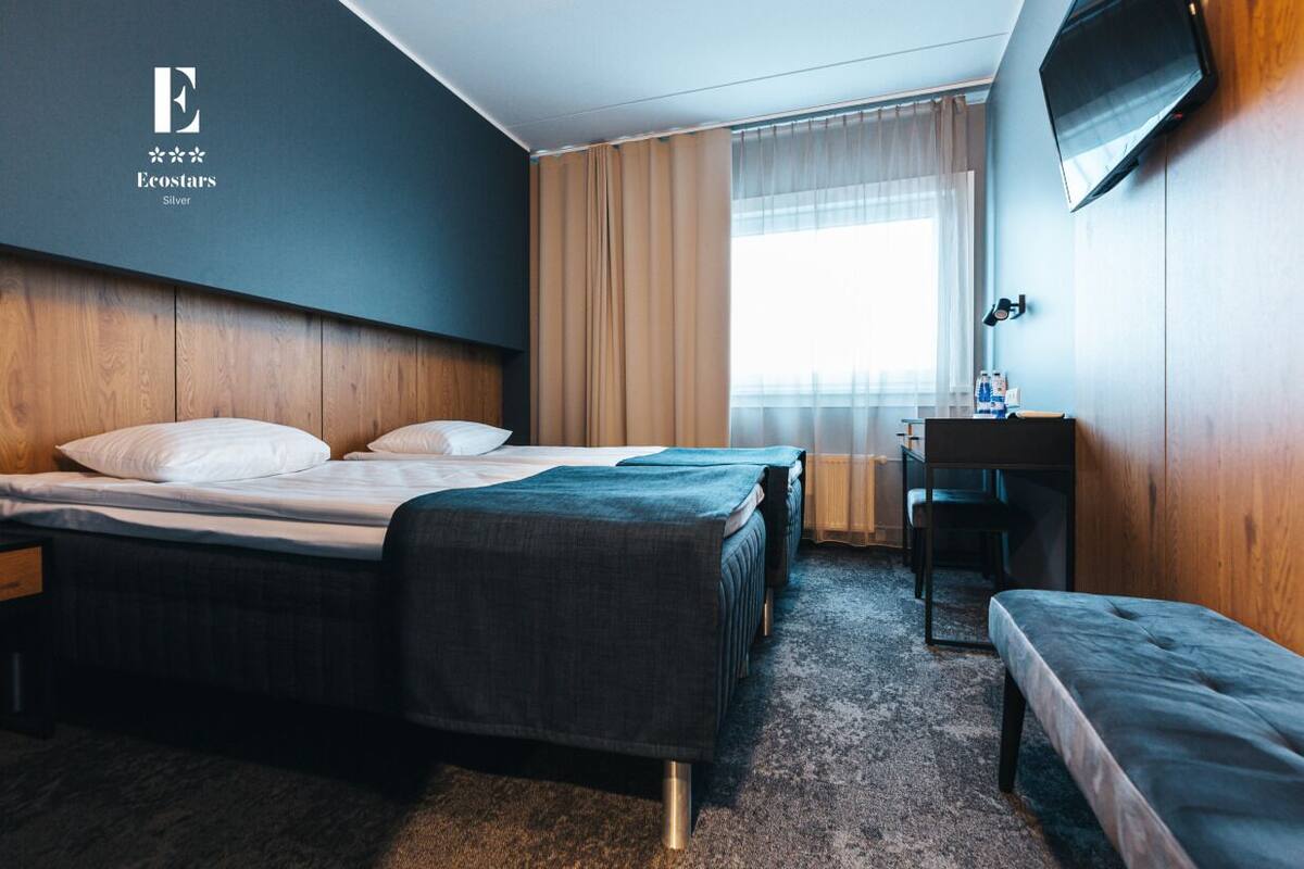 A hotel room with two beds, a desk, a TV, and a window with curtains.
