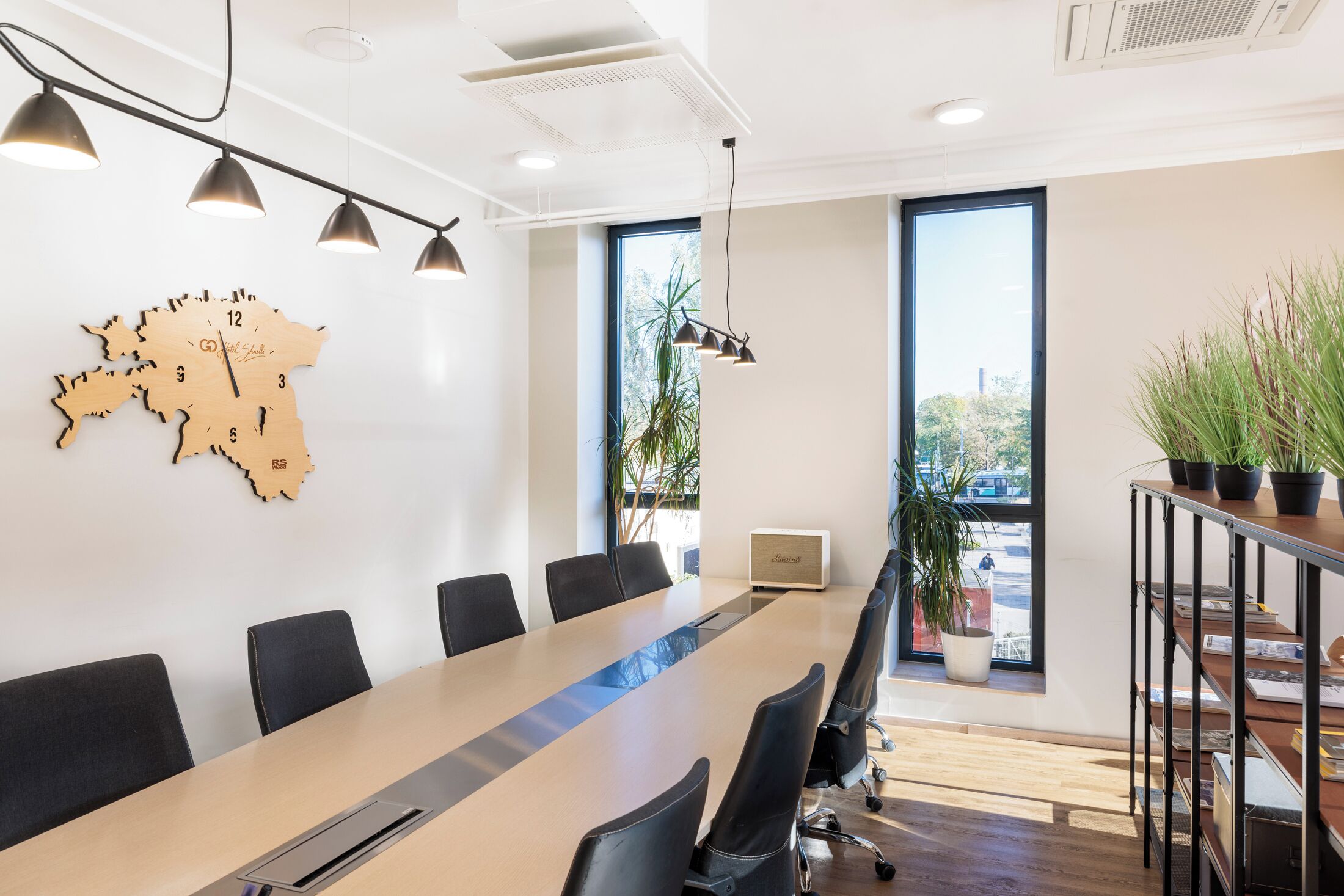 A conference room with a long table, black chairs, pendant lights, a map clock, and large windows.