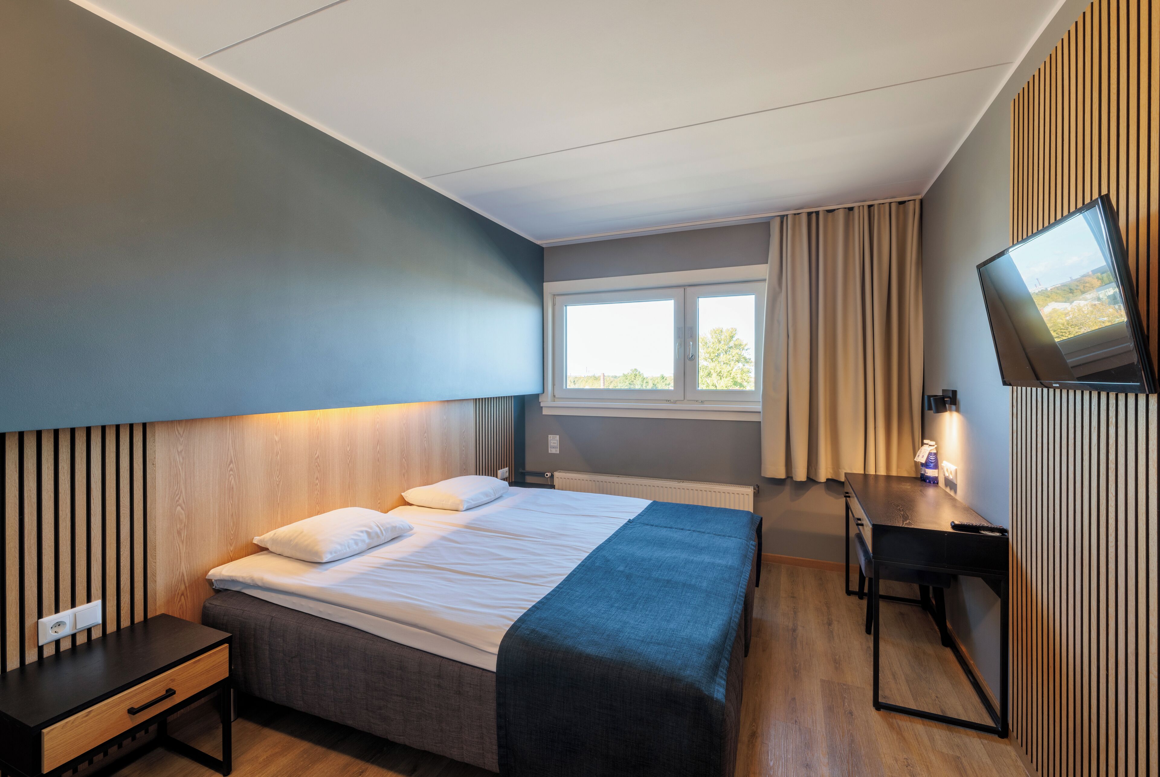Ein modernes Hotelzimmer mit Bett, Nachttisch, Schreibtisch und Fernseher.