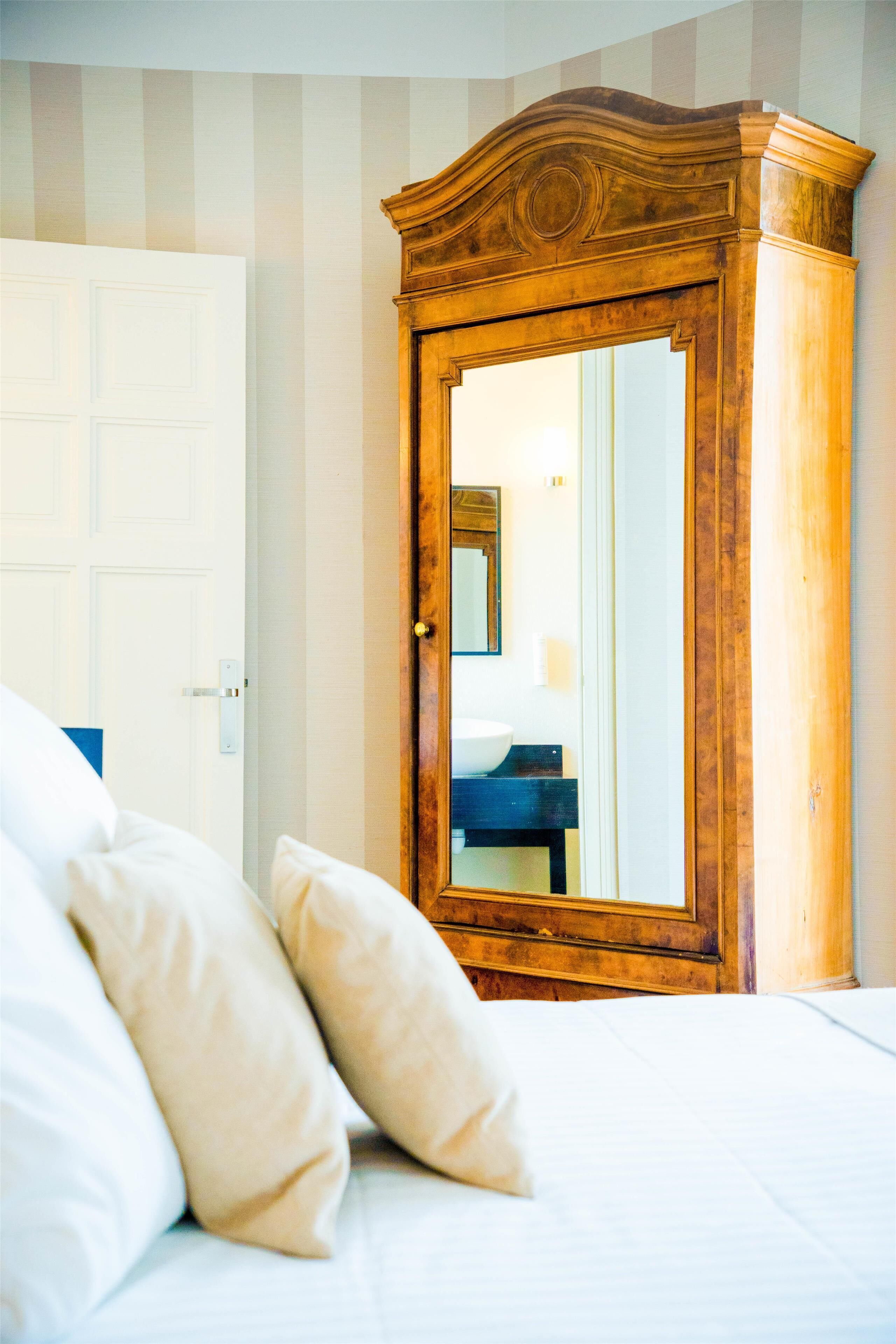 Un dormitorio con un armario de madera, una cama con ropa de cama blanca y una puerta que da a un baño.