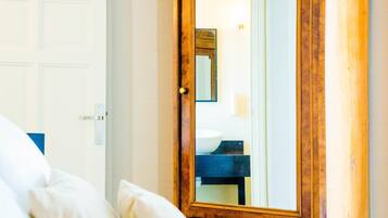 Un dormitorio con un armario de madera, una cama con ropa de cama blanca y una puerta que da a un baño.