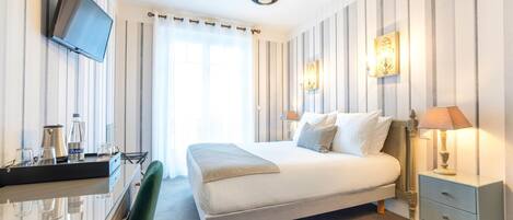 Une chambre d’hôtel comprenant un lit, une table de chevet, une lampe, une télévision et un bureau avec une chaise.