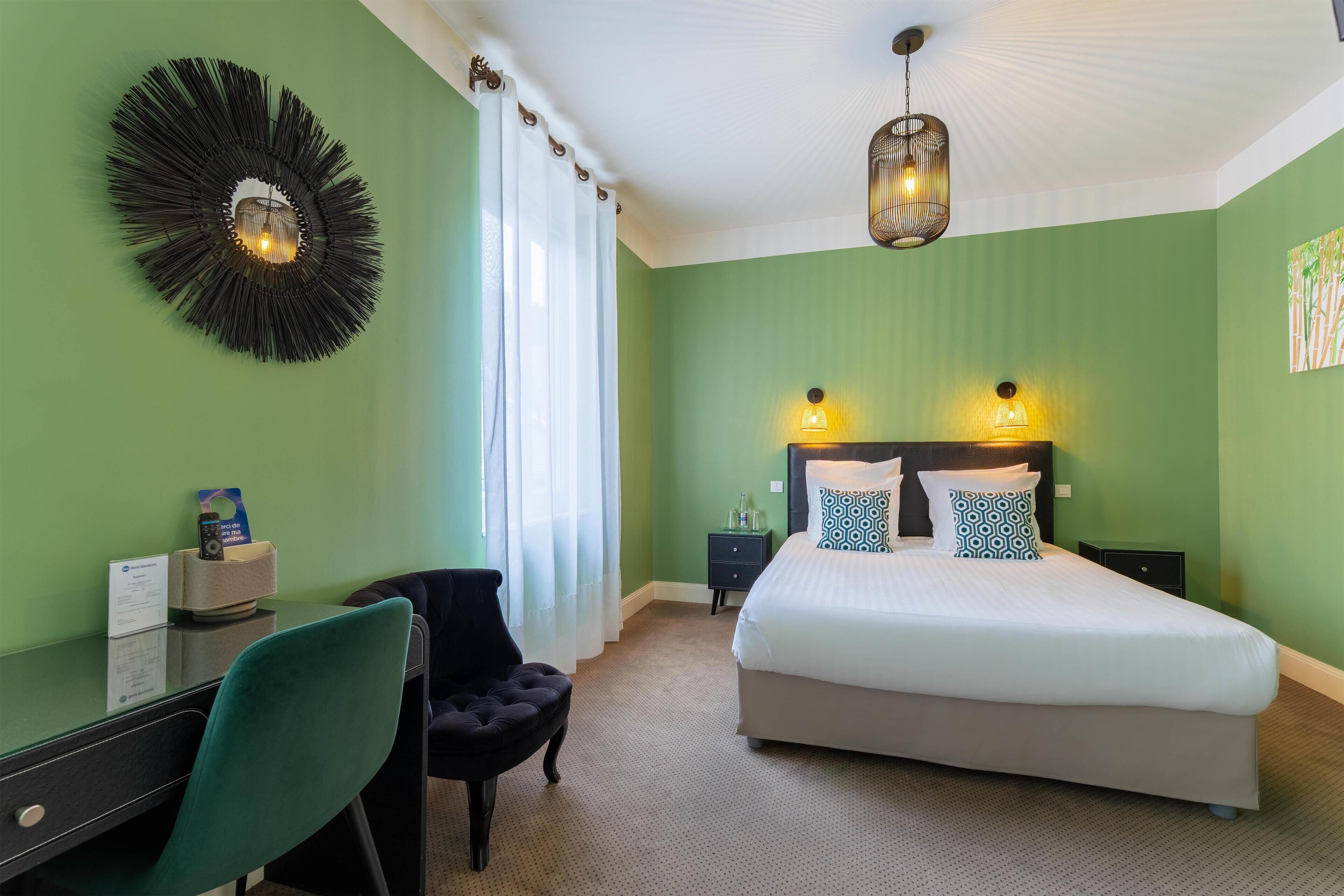 A bedroom with a bed, a desk, a chair, and a wall-mounted light fixture.