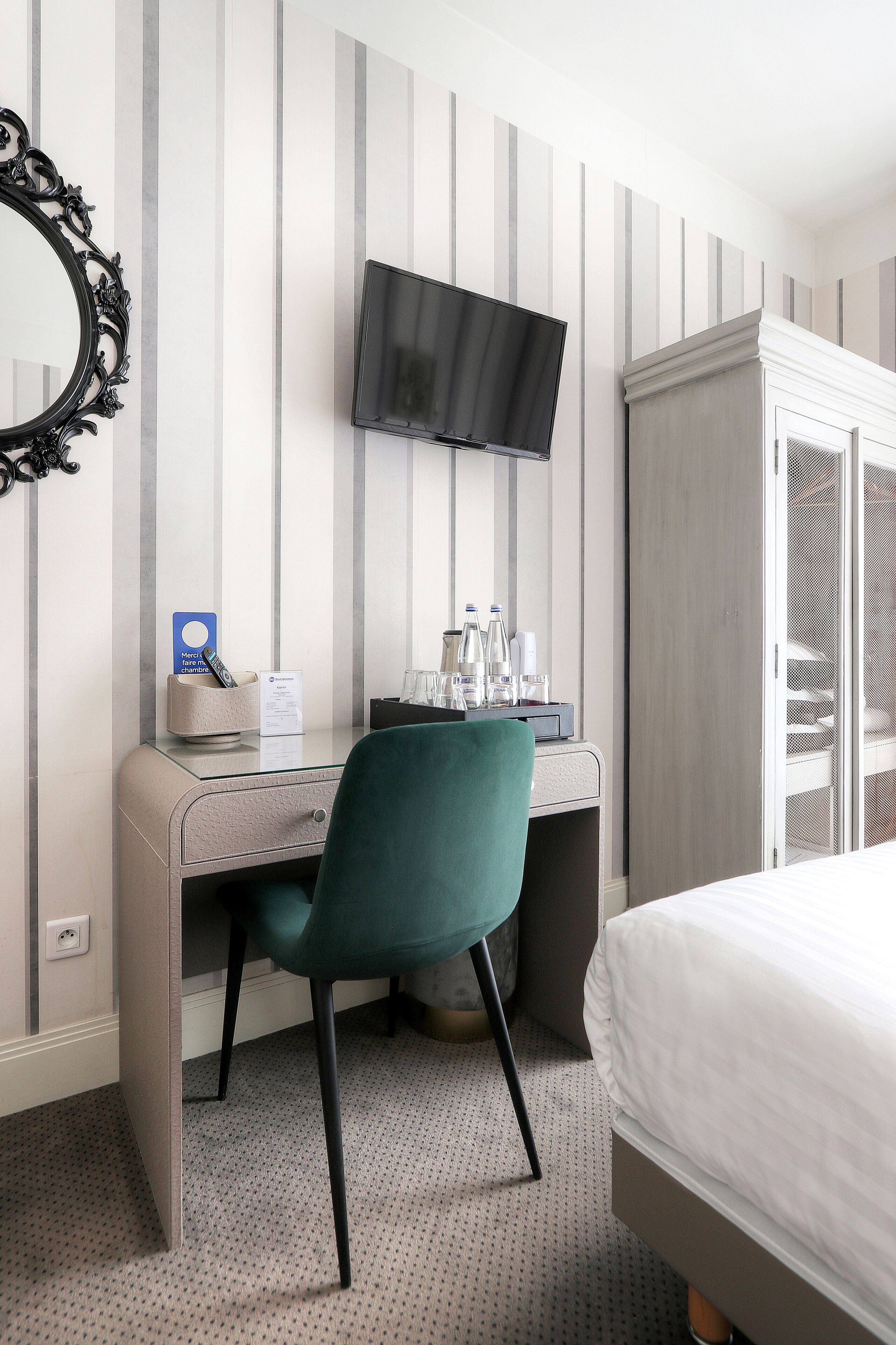 Una habitación de hotel con cama, escritorio, silla, televisor y armario.