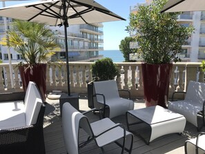 Un balcón con asientos exteriores, plantas en macetas y vista al mar.