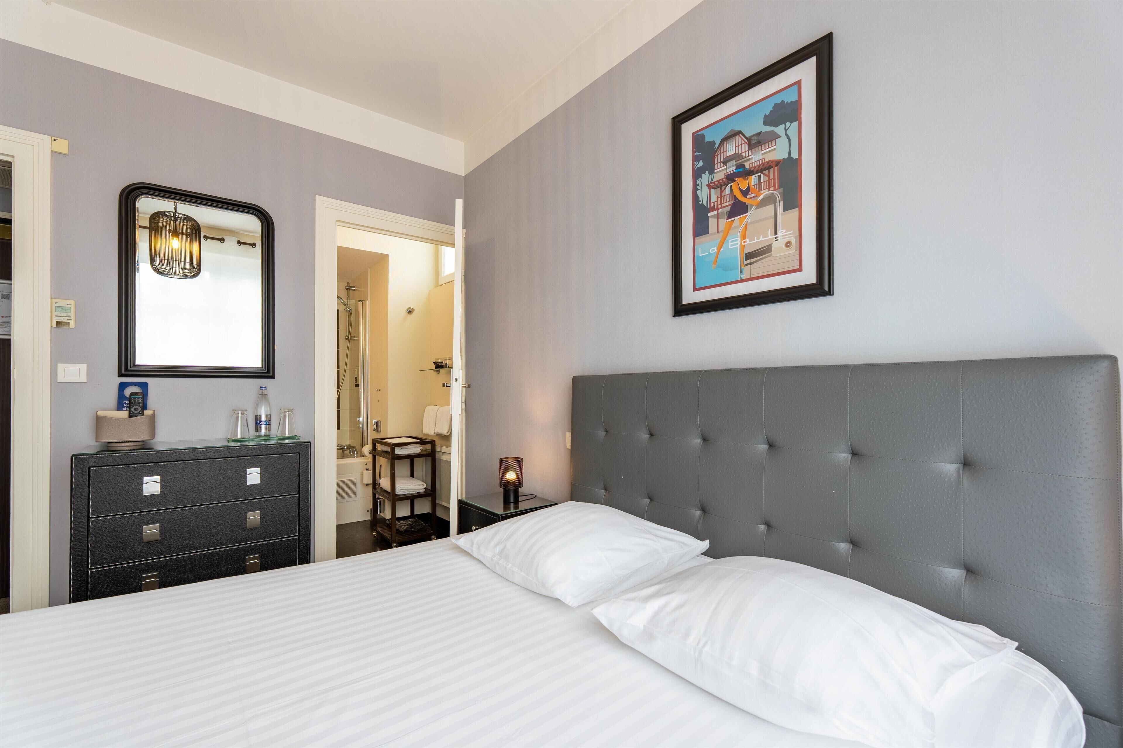 A hotel room with a large bed, a dresser, a mirror, a framed picture on the wall, and a door leading to another room.