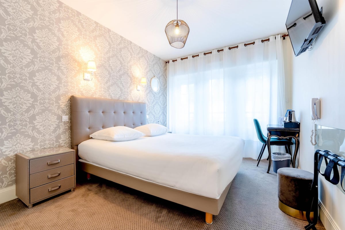 A neatly arranged hotel room with a large bed, bedside lamps, a desk, and a chair.