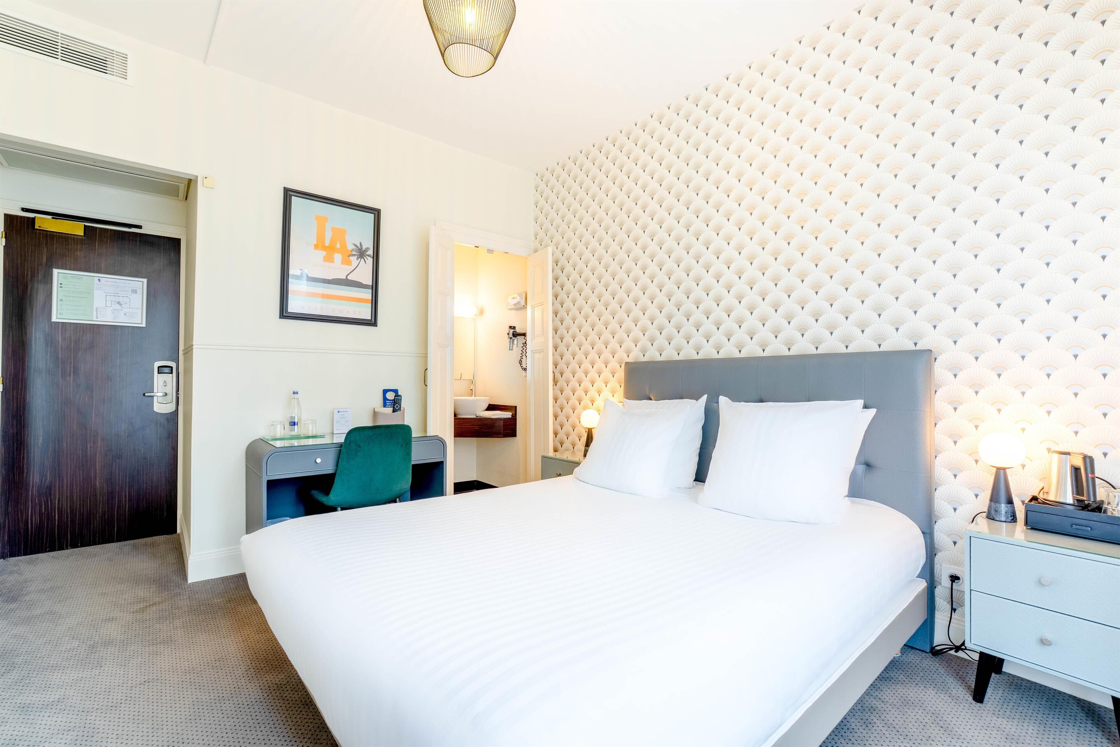 A hotel room with a large bed, a desk with a chair, a nightstand, and a wall with a textured pattern.