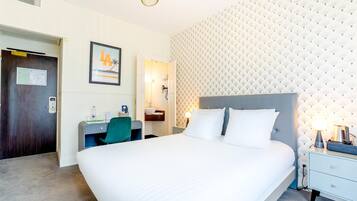 Habitación de hotel con una cama grande, un escritorio con una silla, una mesita de noche y una pared con textura.