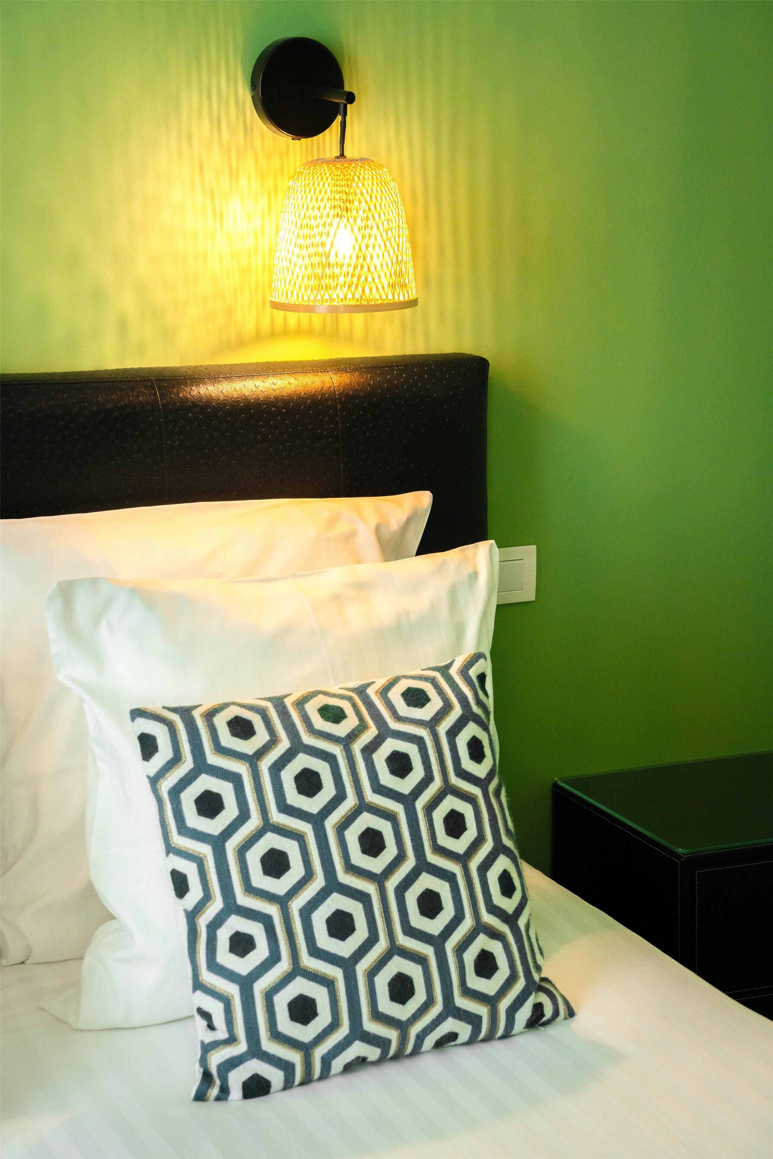 A neatly made bed with white and patterned pillows, a black headboard, and a wall-mounted lamp.