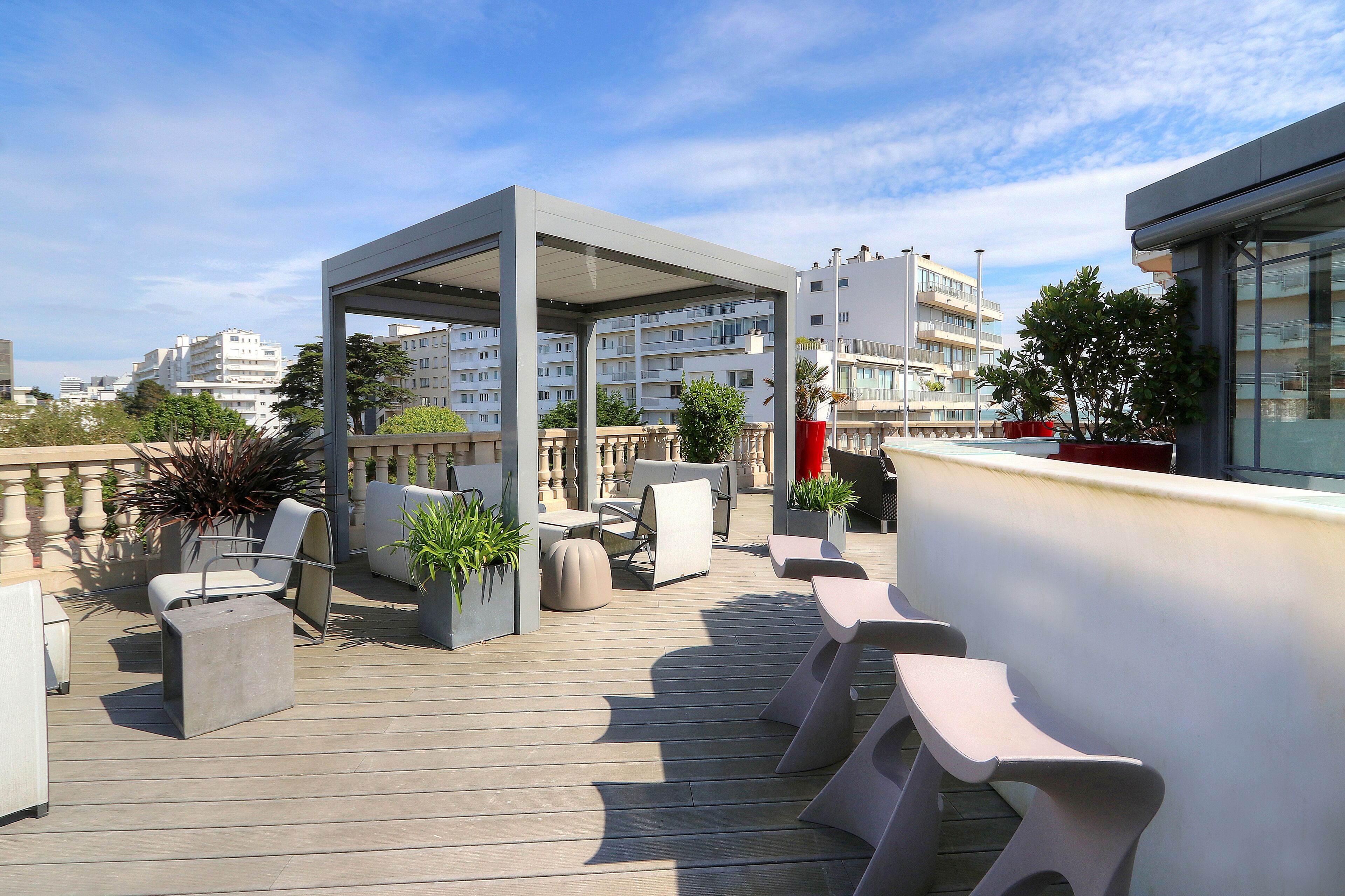Terraza en la azotea con mobiliario exterior, plantas en macetas y vistas de edificios circundantes.
