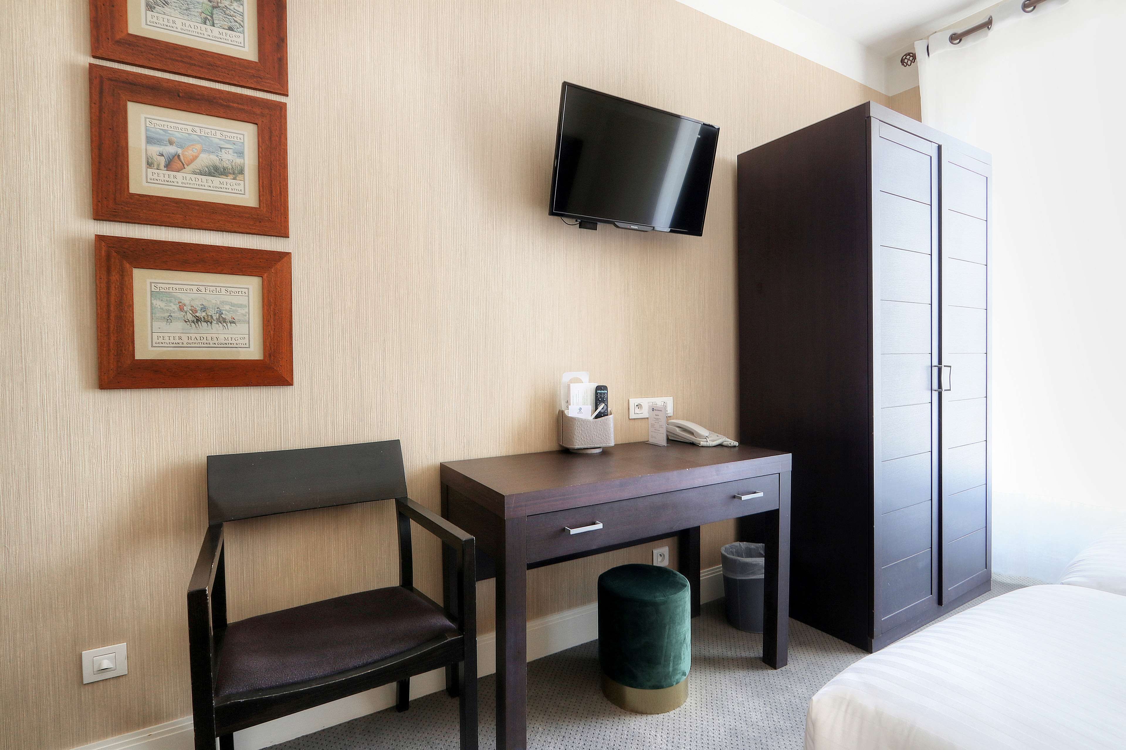 A hotel room with a bed, a desk with a chair, a TV mounted on the wall, and a wardrobe.