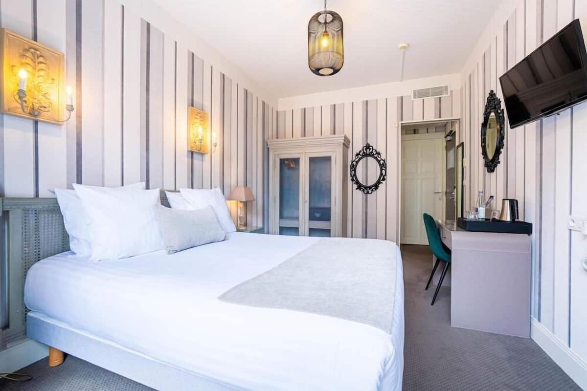 A hotel room with a large bed, a desk, a chair, a TV, and a wardrobe.