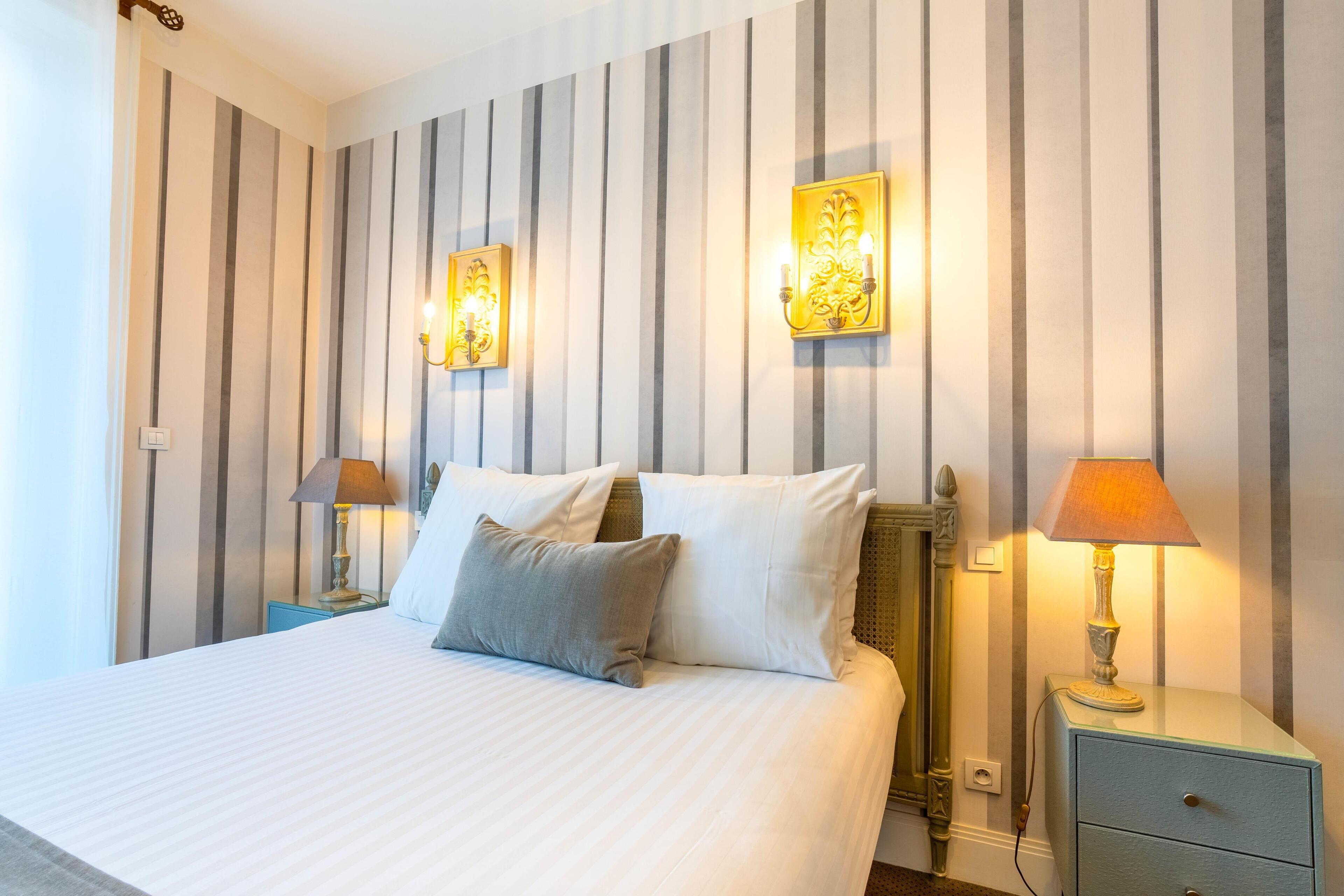 A hotel room with a large bed, two bedside tables, and a nightstand with a lamp.