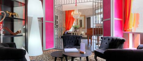 Un moderno vestíbulo de hotel con sillas tapizadas negras, una mesa redonda con un libro y un menú, una lámpara blanca grande y un candelabro.