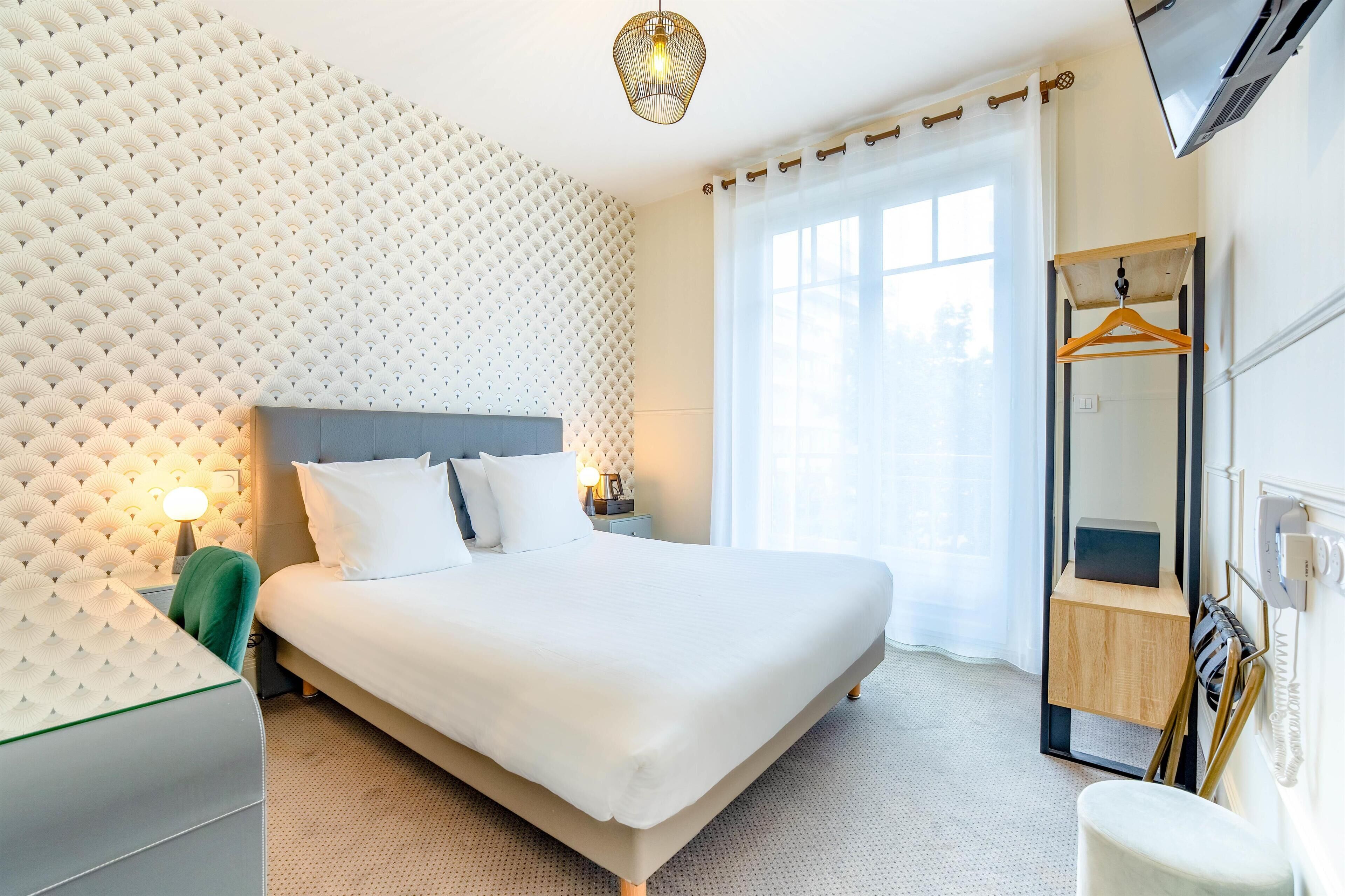 A modern hotel room with a large bed, a headboard with a textured pattern, a bedside table with a lamp, and a mirror with a wooden frame.