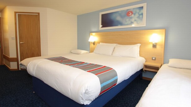 A hotel room with a double bed, two bedside tables, a wooden headboard, and a painting on the wall. - Travelodge Dunfermline (Dunfermline)
